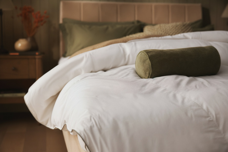 Close-up of a Sleepeezee duvet and green bolster pillow in soft, moody light